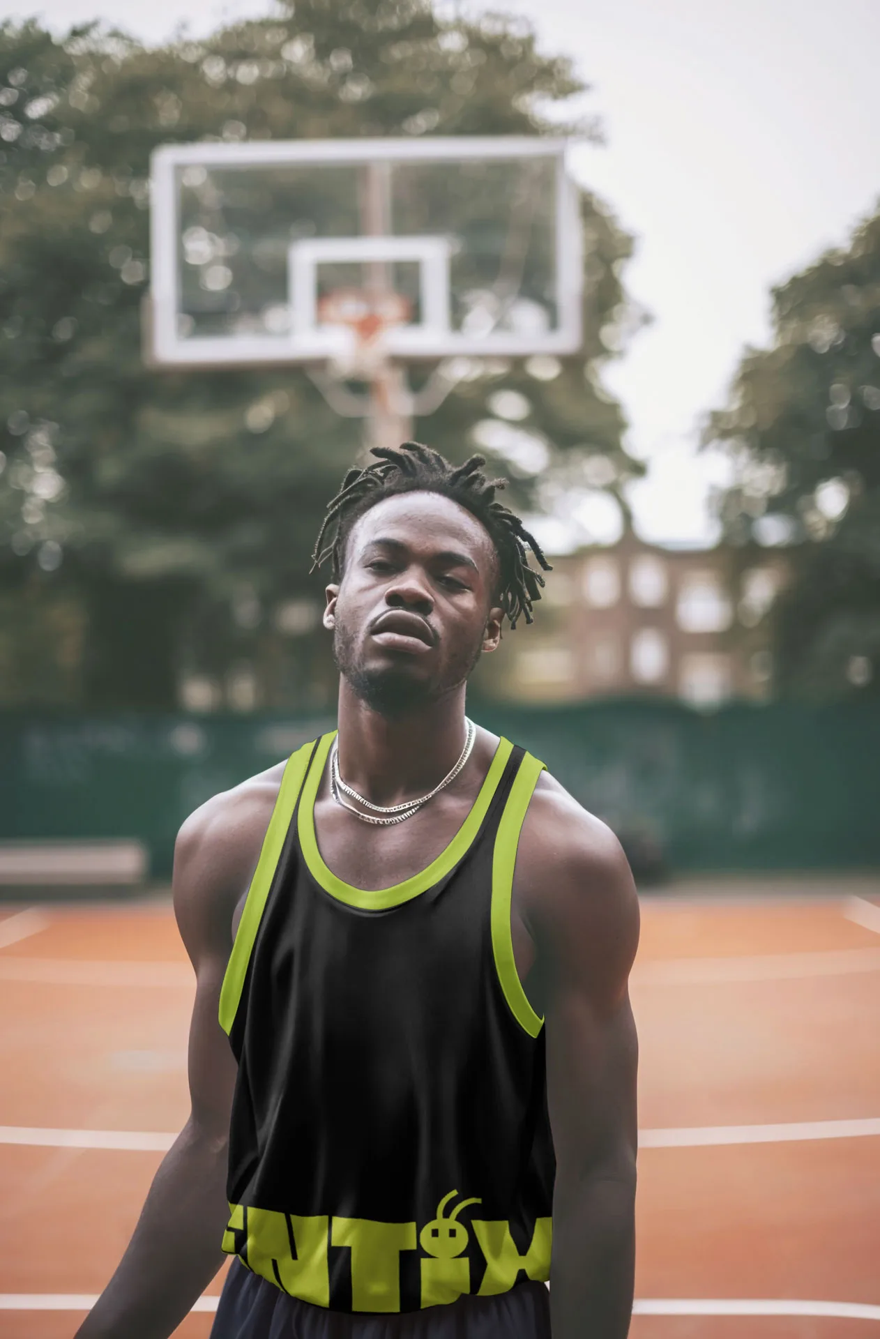Uomo su un campo da basket con canotta nera bordata di verde acido e logo Entix, canestro sullo sfondo.