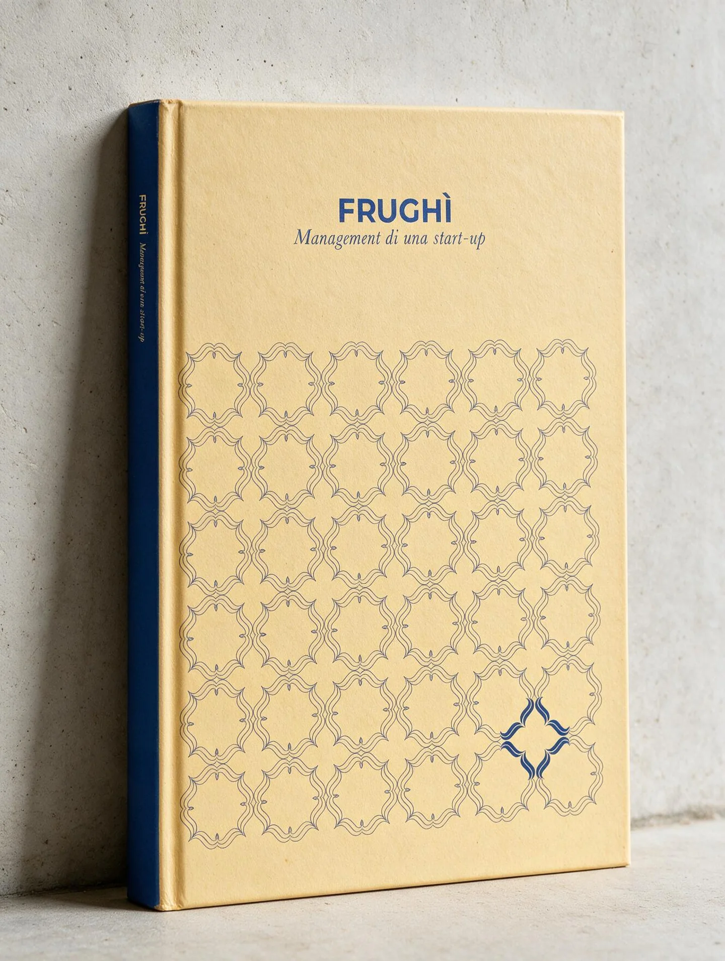 Mock-up del libro Frughì in piedi contro una parete chiara, con il dorso blu a vista: sul fondo giallo burro, la texture e il titolo FRUGHÌ con il sottotitolo Management di una start-up.