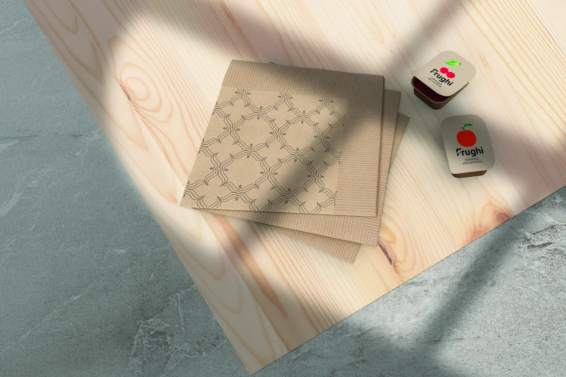 Set per la colazione in albergo su un piano di legno chiaro: tovaglioli in carta Kraft con la texture stampata a filo e due porzioni monodose sigillate, una alla ciliegia e una alla mela.