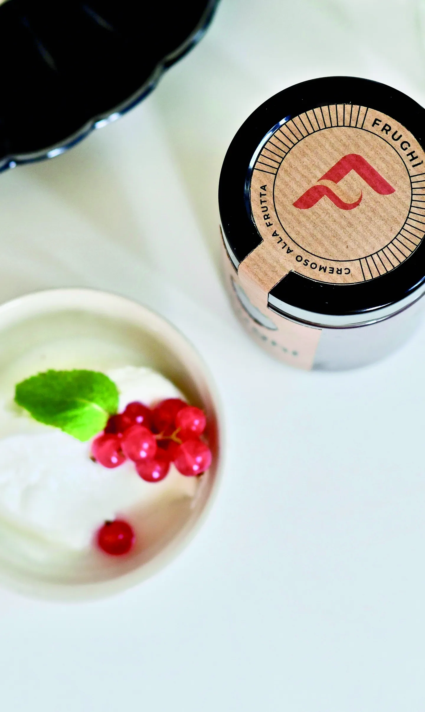 Vasetto ripreso dall'alto accanto a una coppa di gelato: sul tappo nero il sigillo tondo in carta Kraft, con la F rossa al centro, la raggiera di filetti e il nome che corre lungo il bordo.