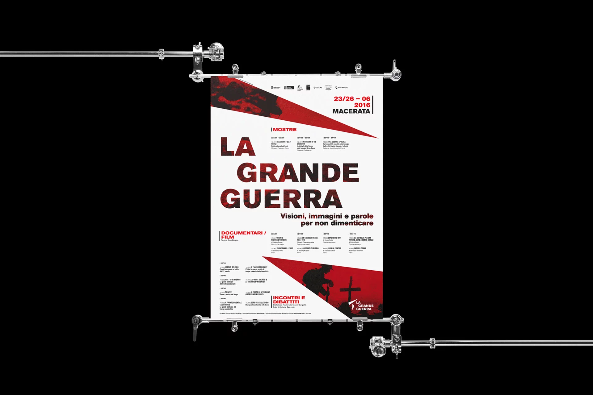Manifesto bianco appeso a due barre metalliche su fondo nero: il titolo LA GRANDE GUERRA in nero e rosso, il sottotitolo Visioni, immagini e parole per non dimenticare, e il programma diviso in mostre, documentari e incontri. In alto a destra le date 23/26 – 06 2016 e la città, Macerata.