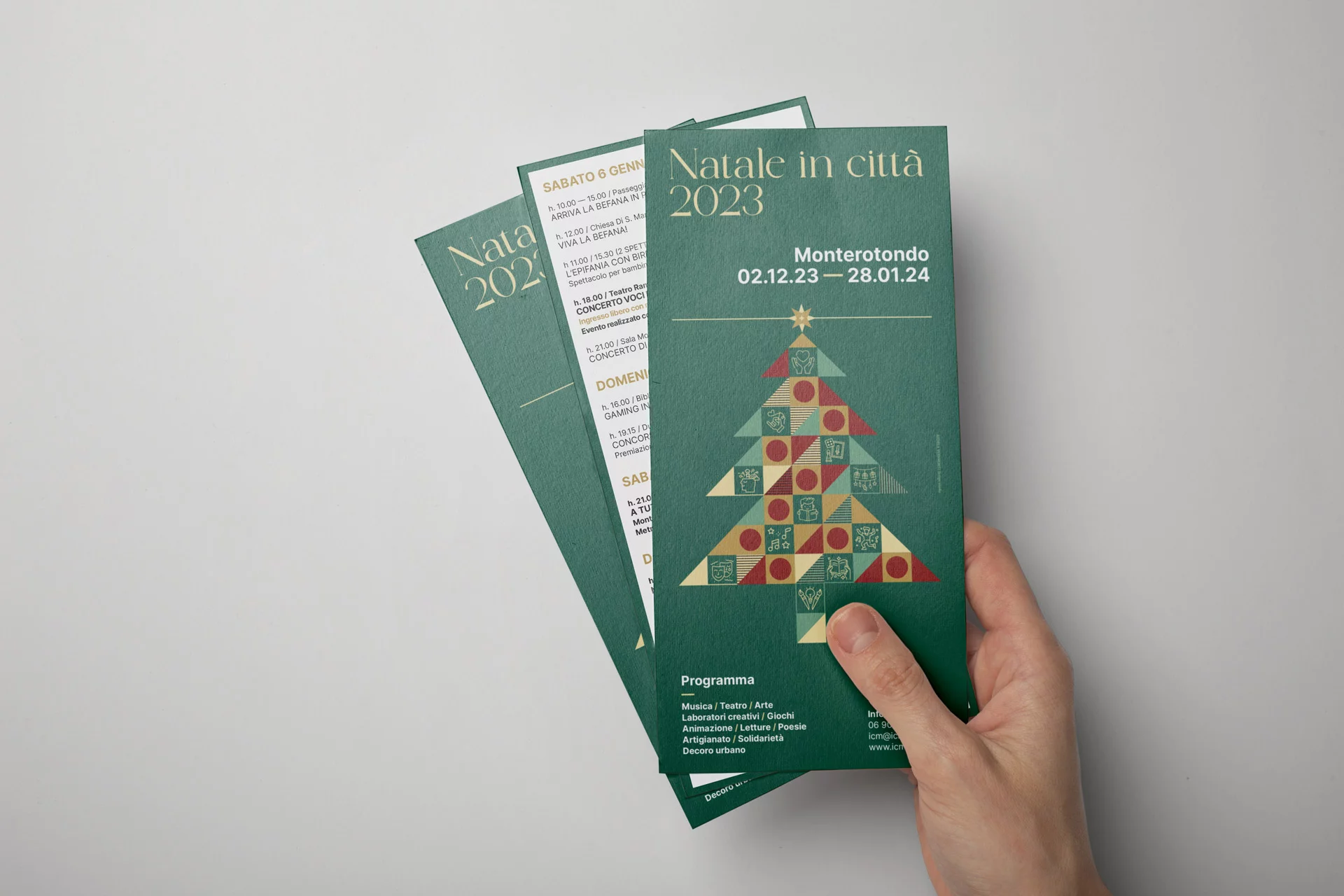 Tre pieghevoli verdi tenuti a ventaglio in una mano su fondo grigio: davanti la copertina con l'albero e le date, dietro una pagina bianca con il calendario degli appuntamenti giorno per giorno.
