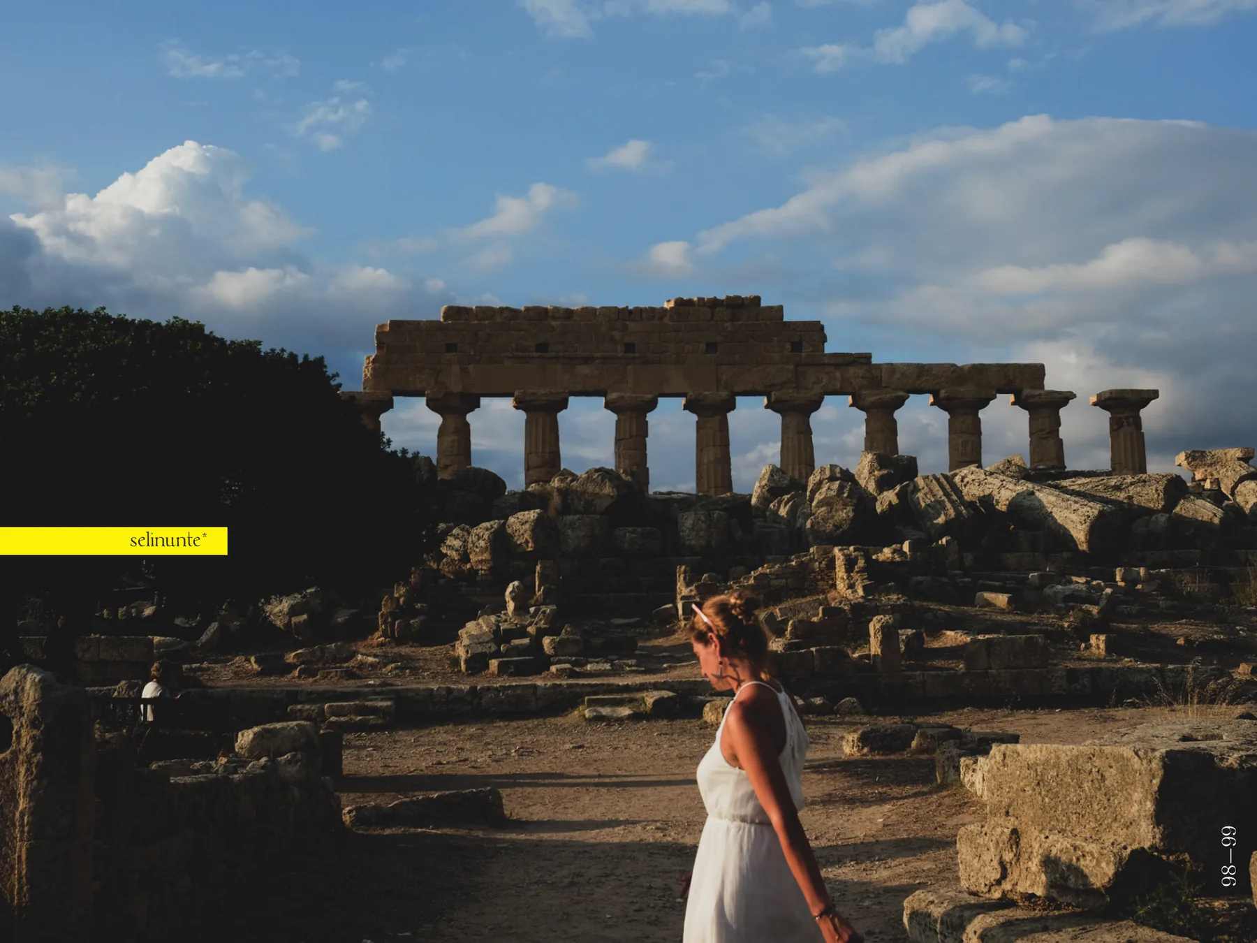 Doppia pagina 98—99: il tempio di Selinunte al tramonto sotto un cielo azzurro con nuvole alte, la stessa ragazza in bianco di spalle in primo piano, e la didascalia selinunte* dentro una barra gialla sul bordo sinistro.